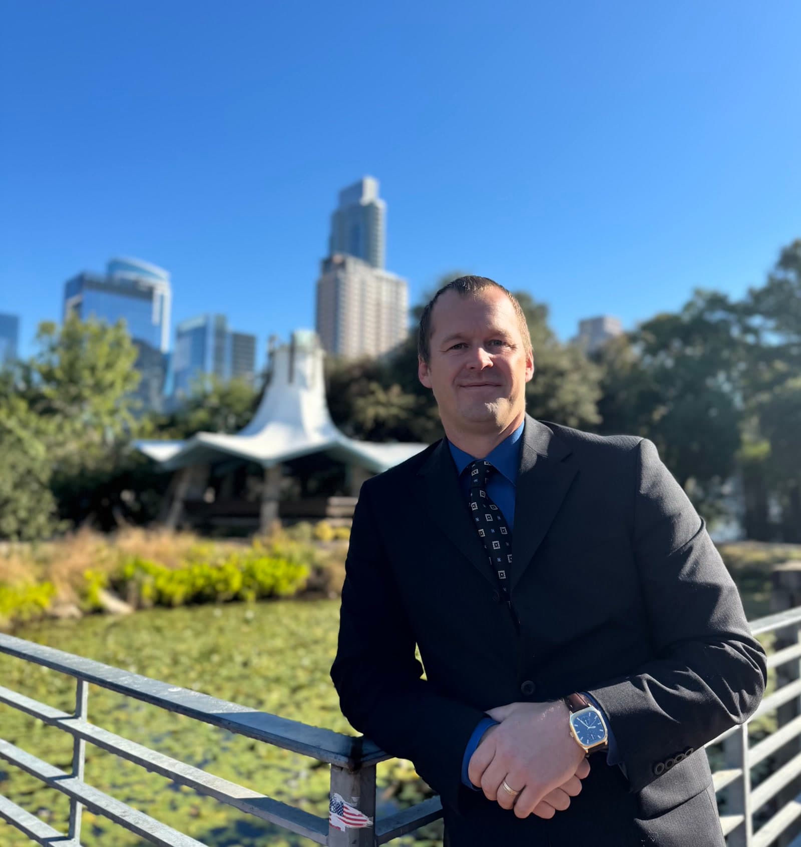 Andrew M. Crawford in a dark suit on a bridge in front of the Austin skyline.